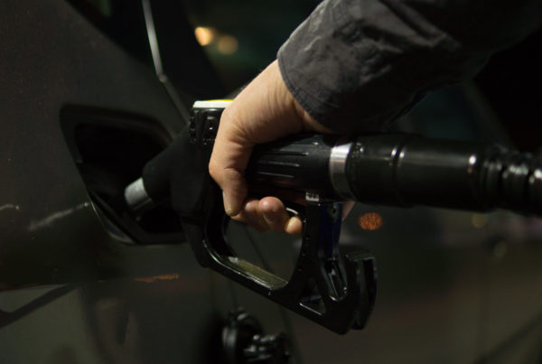 A hand pushes a gas pump nozzle into a vehicle