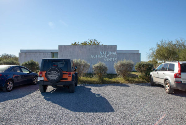 the front entrance of the national butterfly center in concrete brick and silver lettering with a jeep parked in front
