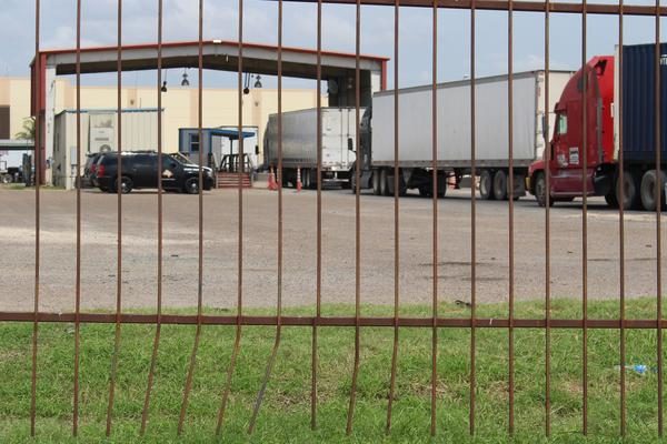 view through a fence at a line of trucks headed toward the port of entry checkpoint