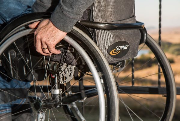 Closeup of a wheelchair user's hand gripping the spokes of their chair.