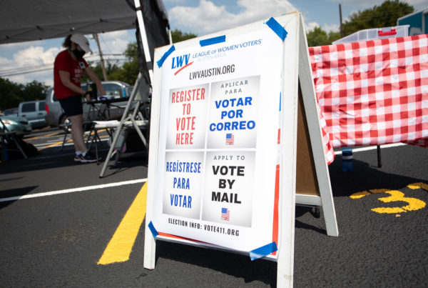 an a-frame sign with signs posted on it about voting by mail and registering to vote, in english and spanish