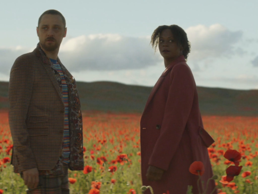 Two people stand in a field of red poppies.
