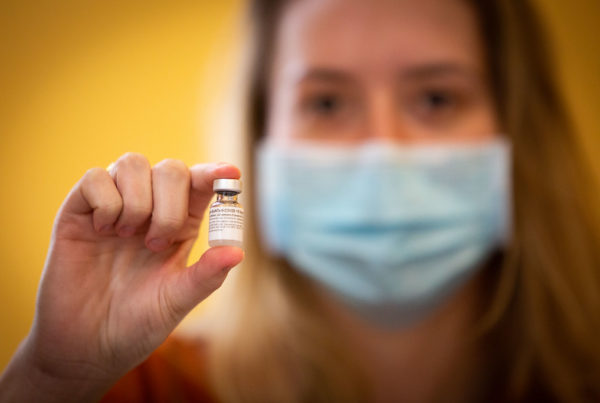 a woman holding a vial of a vaccine