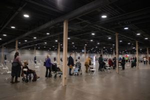 a line of people, mostly in wheelchairs with their caretakers, waiting for vaccines in a large convention hall