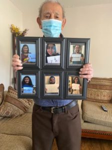 Navarro's Guelo wears a mask as he holds a frame with multiple pictures of loved ones.
