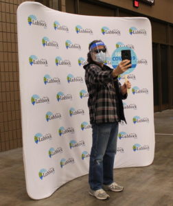 a man standing in front of a city banner taking a selfie photo after getting the covid-19 vaccine