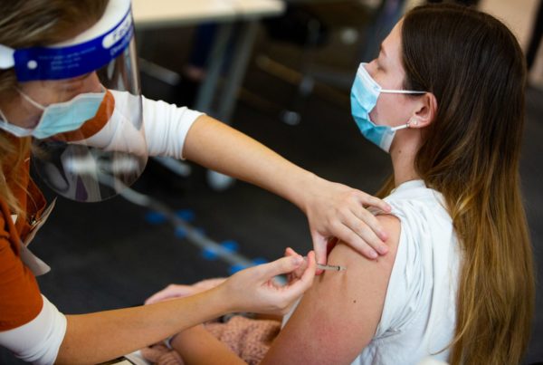 a woman getting a vaccine from a person wearing a face shield