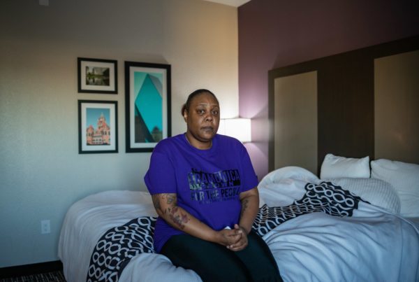 a woman in a purple shirt sitting on a hotel bed
