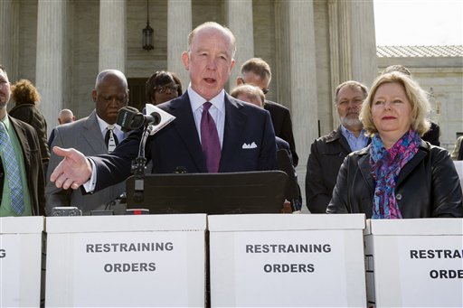 a man standing in front of the U.S. Supreme Court building speaking at a microphone with people behind and next to him