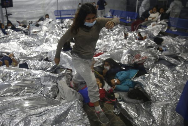a young girl in an immigrant detention facility with silver foil blankets surrounding her
