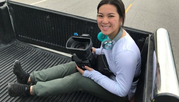 A woman in the back of a pickup holding a video camera