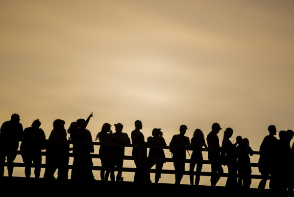A long shot of a large group of people in silhouette on a bridge.