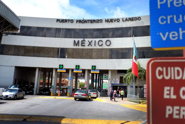 a three story building with tunnels underneath at the border to Mexico with cars driving under and a sign that says mexico on the building