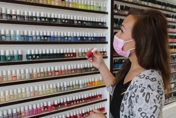 a nail salon owner in front of a wall of nail polish bottles