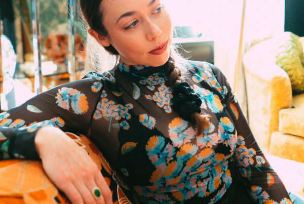 singer sarah jarosz sitting on a cough wearing a black top wtih a colorful print