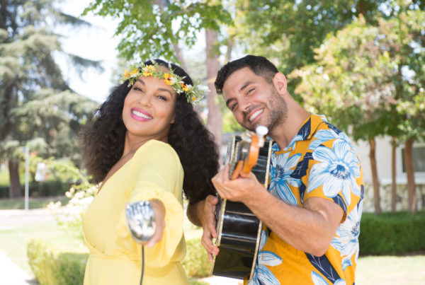 a woman holds a microphone and a man plays a guitar on the sidewalk
