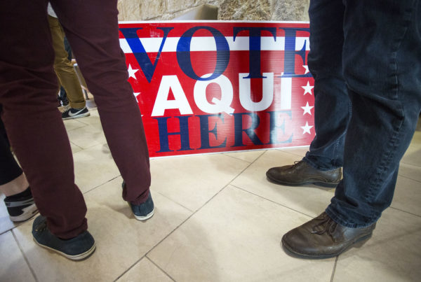 People stand in line next to a sign that says "vote aqui here"