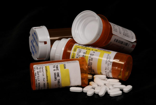 A bunch of opioid pills like hydrocodone in their pharmacy bottles.