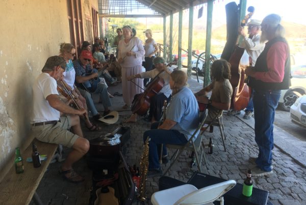 About 15 musicians of a wide age range play guitars, fiddle, the flute and upright base on the porch of the Terlingua recording studio.