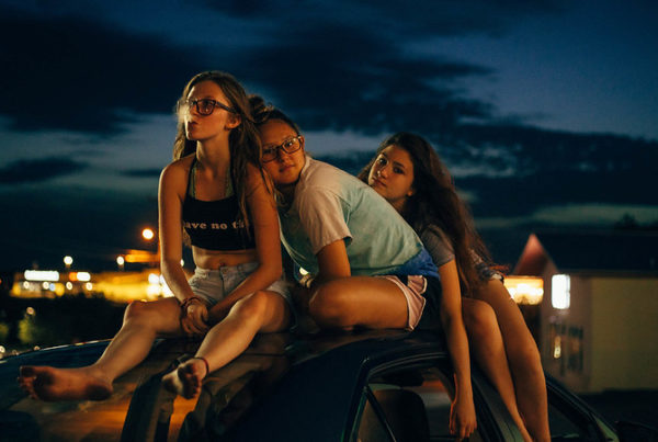 three teenage girls sit atop a vehicle at dusk