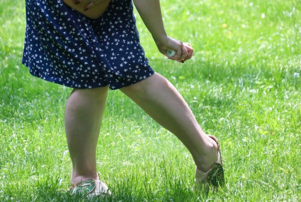 a person in a dress sprays bug spray on their legs while standing in green grass