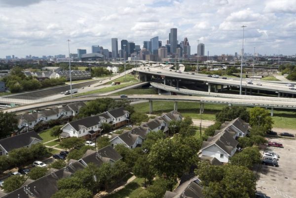 an overhead view of homes next to a highway. Beyond is the Houston skyline.