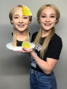 Cake artist Natalie Siderf poses next to her selfie cake – a realistic bust of her blonde head with one slice missing.