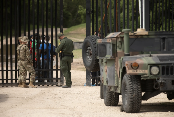 A group migrants waits at a gate near the U.S. and Mexico border in Del Rio on July 22, 2021. The group turned themselves over to the National Guard and Customs and Border Protection officials.