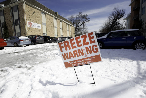 a white yard sign with red lettering that says "freeze warning" staked into snow on the yard of an apartment building