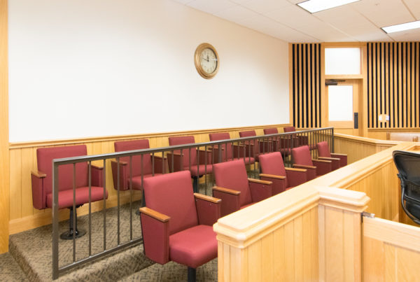a jury box in a courtroom with red cushioned chairs and a brown railing in between two rows of several seats