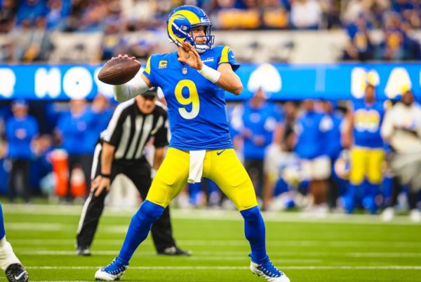 a Rams quarterback wearing a gold and blue uniform, arm cocked for a pass