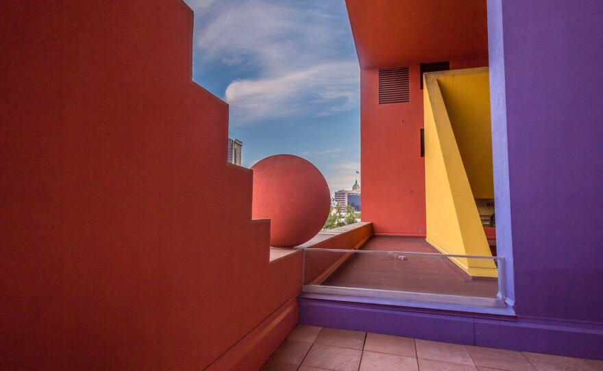 a red wall with stairstep edges, a large red ball sculpture, a yellow triangular wall and a rectangular purple wall, all architectural elements of san antonio public library
