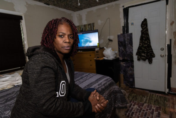 a woman sitting on a bed inside her home, she's wearing a black sweatshirt