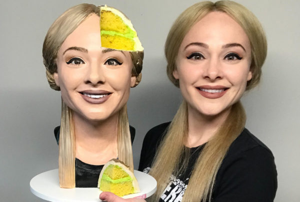 Cake artist Natalie Siderf poses next to her selfie cake – a realistic bust of her blonde head with one slice missing.