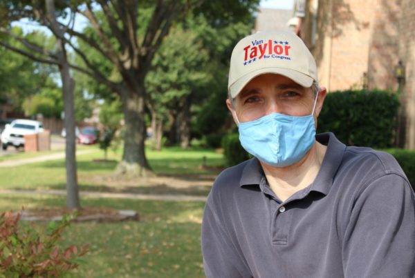 a man wearing a blue polo shirt, blue face mask and a brown hat that says Van Taylor, with trees and a house in the background