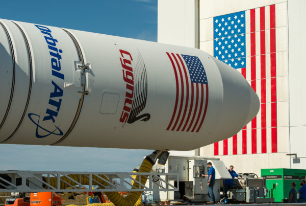 A large rocket lays on its side, on a trailer. It says "Antares" and sports a US flag.