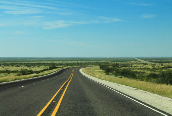 an empty three-lane highway stretches out into a blue-sky horizon