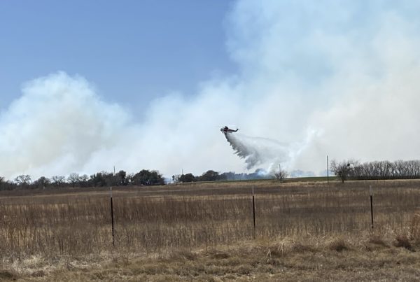 a helicopter drops what appears to be water on a smoking section of rural grassland and trees