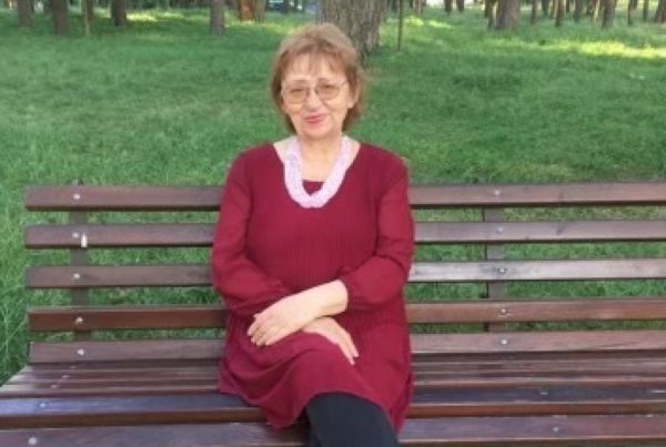 a woman sits smiling on a park bench