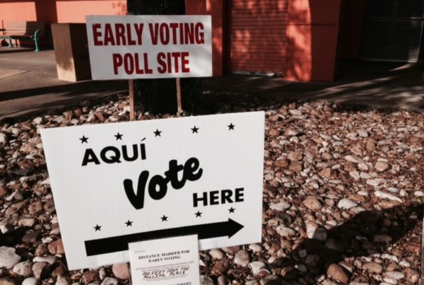 a white sign with black writing that says aqui, vote here, staked into rocks