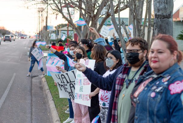 people lined up on the side of the road with signs in support of transgender people and with signs that have the pink blue and white stripes in support of transgender rights