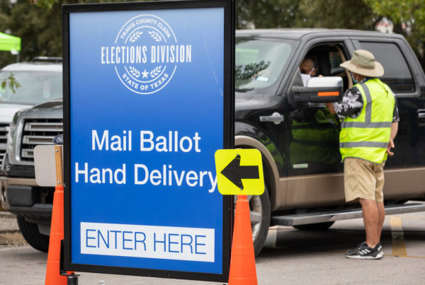 a large blue sign that says mail ballot hand delivery enter here, with a large truck behind it and an election official wearing a yellow vest