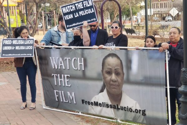 several people standing behind a large banner with a woman's face whose hair is pulled back in a ponytail that says watch the film next to her