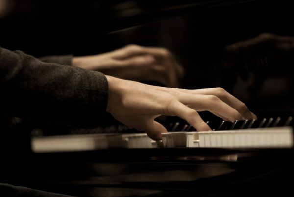 a closeup image of a pianists hands playing the piano with long shirtsleeves