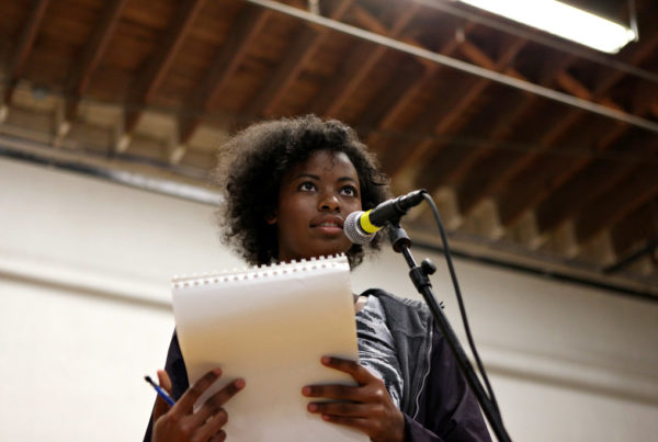 a woman stands at a microphone and holds a pen and notebook