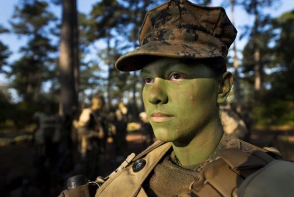 A solider outdoors in fatigues with green paint on her face