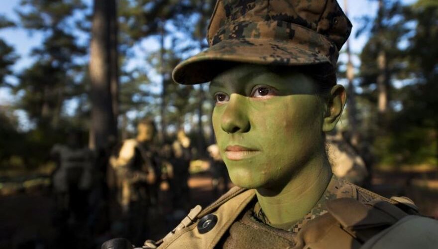 A solider outdoors in fatigues with green paint on her face
