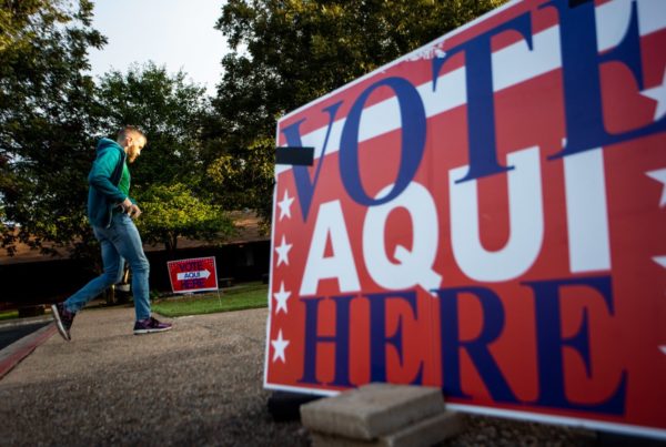 A man walks past a sign that says "vote here/aqui"