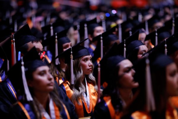 A crowd of graduates in caps and gowns looks ahead during a graduation ceremony.