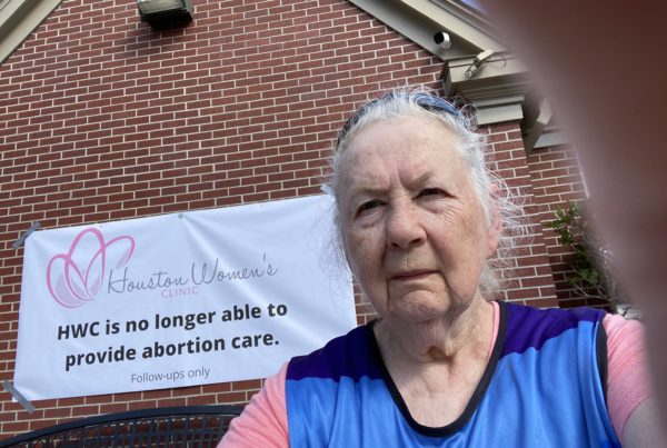 an older woman stands in front of a sign that says "HWC is no longer albe to provied abortion care."